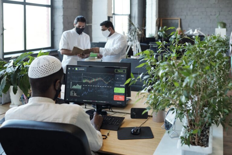 Rear view of young Muslim businessman sitting in front of computer monitor and his two colleagues in office